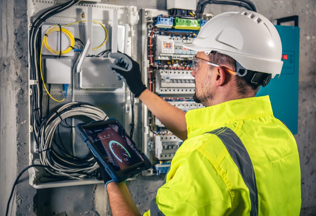 Man, an electrical technician working in a switchboard with fuses. Installation and connection of electrical equipment. Professional uses a tablet.